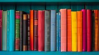 Colorful hardcover books arranged in row on wooden shelf, spines showing vibrant spectrum from turquoise to red and orange, creating rainbow gradient effect. Perfect for education themes.