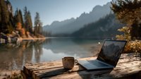 Laptop and coffee cup on wooden table by mountain lake at sunset creating peaceful remote work atmosphere for digital nomads and outdoor office concepts.