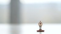 Miniature wooden figurine in meditation pose with raised arms on white surface against soft blurred background for wellness and mindfulness concepts.