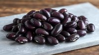 Fresh dark red kidney beans scattered on gray linen napkin against wooden table background, macro food photography for cooking and healthy eating concepts.