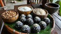 Dark chocolate truffles rolled in coconut flakes served on banana leaf with wooden bowls of nuts, shredded coconut and cocoa powder for homemade confectionery.