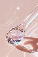 Crystal clear water drop with iridescent reflections on spoon against soft pink background, capturing light and rainbow effects in macro photography.