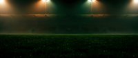 Empty soccer stadium at night with dramatic lighting and green grass field ready for match or training session.