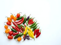 Assorted fresh chili peppers in red, yellow, orange and green varieties arranged on white background for culinary and food styling projects.
