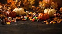 Autumn harvest display with pumpkins, colorful candy, nuts and fall leaves on rustic wooden table for seasonal decorating and holiday celebrations.