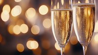 Two elegant champagne flutes filled with sparkling golden champagne against warm bokeh lights background for celebration and festive occasions.