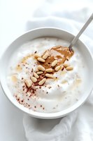 Creamy white yogurt bowl topped with drizzled honey, roasted pine nuts and cocoa powder in minimalist style on bright background. Healthy breakfast concept.