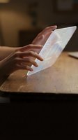 Hands interacting with futuristic holographic display showing data charts and graphs on wooden surface in modern office environment.