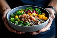 Fresh quinoa buddha bowl with salmon, mango, broccoli, pomegranate seeds and mixed greens served in ceramic bowl, held in hands. Food photography.