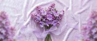 Fresh lilac bouquet wrapped in delicate tissue paper on soft fabric background for spring celebrations and romantic occasions.