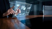 Young male professional in business attire interacting with holographic digital interface displaying analytics, charts and data icons on wooden desk in modern office environment.