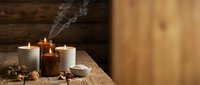 Aromatherapy essential oil bottle with burning candles and dried herbs on wooden surface for wellness and relaxation.