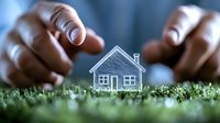 Small paper house sketch placed on green moss between African American male hands, representing real estate, home ownership and property investment concept.