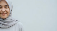 Young Muslim woman in light gray hijab smiling warmly against neutral background. Professional portrait for diversity, inclusion and multicultural content.