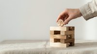 Hand placing wooden block with brain icon onto jenga tower representing strategic thinking, problem solving and mental skills development for business concepts.