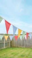Colorful fabric bunting flags hanging in backyard garden with wooden fence and blue sky for outdoor party celebration and festive decoration.