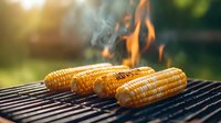 Grilled corn on the cob with smoke and flames on barbecue grate during summer cookout. Golden kernels charring over hot coals in sunlit outdoor setting.