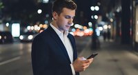 Young professional businessman using smartphone on city street at night with bokeh lights background for business communication and urban lifestyle.