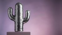 Shiny silver sequined cactus sculpture on pedestal against purple gradient background for modern home decor and desert-themed interior design concepts.
