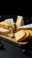 Gourmet cheese platter with variety of artisanal cheeses on wooden cutting board, dark grapes scattered around for elegant appetizer presentation.