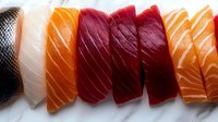 Fresh assorted sashimi slices including salmon, tuna and white fish arranged in row showing vibrant colors and textures of raw fish for Japanese cuisine.
