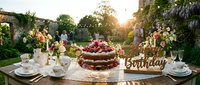 Elegant outdoor birthday celebration with a rustic naked cake, fresh flowers, and vintage tableware in a sunlit garden setting.