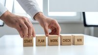 Business professional arranging wooden blocks spelling START PLAN WORK CHECK WIN showing project management workflow and strategic planning process.