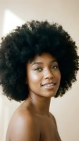 Young African American woman with natural afro hairstyle smiling confidently in soft natural lighting for beauty and wellness campaigns.