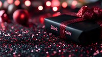 Black gift box with red glitter ribbon against dark background with bokeh lights and scattered sparkles, creating festive holiday shopping atmosphere.