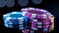 Colorful casino poker chips stacked in piles with blue and pink neon glow effect against dark background, creating dramatic gaming atmosphere.