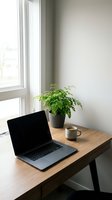 Minimalist home office workspace with laptop, coffee mug and green plant on wooden desk by window. Clean modern interior design for remote work productivity.