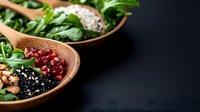 Fresh salad bowls with arugula, pomegranate seeds, black beans, and pine nuts on dark background, healthy vegetarian meal preparation concept.