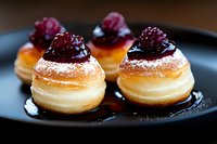 Mini cream puffs topped with fresh raspberries and powdered sugar on black plate, close up view of delicate French pastries with glossy berries.