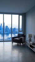 Modern high-rise apartment interior with black leather armchair, floor-to-ceiling windows overlooking urban skyline and waterfront cityscape, minimalist decor, polished concrete flooring.