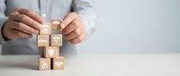 Professional businessman arranging wooden blocks with business icons in strategic formation on desk, representing corporate planning and organizational structure.