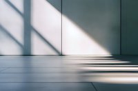 Diagonal window light and shadows cast on minimalist white wall and floor creating geometric patterns in empty modern interior space.