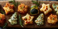 Festive appetizers with star and tree shapes, crispy fried bites, and cheese canapes arranged on wooden board with fresh rosemary garnish.