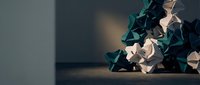 Modern geometric low poly sculpture with angular faceted surfaces in teal and beige tones on wooden surface against blurred background for contemporary decor.