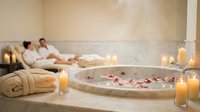 Luxury spa bathroom with romantic jacuzzi, rose petals, candles and couple relaxing on loungers creating intimate wellness atmosphere for vacation retreat.