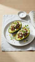 Halved avocados topped with crumbled bacon, crumbly cheese, fresh herbs and olive oil drizzle on white plate for healthy lunch or appetizer recipes.