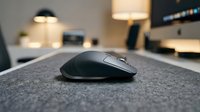Wireless computer mouse on gray desk pad in modern office workspace with blurred background lighting and equipment.