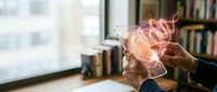 Businessman hands holding glowing brain hologram in modern office with books, representing artificial intelligence, innovation and creative thinking concepts.