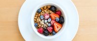Overhead view of granola cereal bowl with mixed fresh berries, strawberries, raspberries and blueberries in white dish on wooden surface for breakfast.