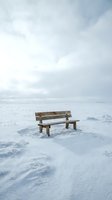 Wooden bench sitting alone in snowy winter landscape with overcast sky, conveying solitude and contemplation for editorial and conceptual projects.