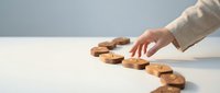 Business professional arranging wooden question mark symbols on white desk representing problem solving and decision making process.