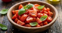 Fresh diced tomatoes with basil leaves in wooden bowl on rustic table for cooking and meal preparation.