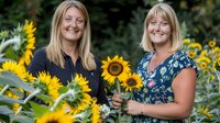 Cheerful Caucasian women with blonde hair smiling in sunflower field, wearing casual summer clothes. Natural outdoor portrait with bright yellow blooms.