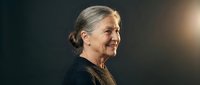 Senior Caucasian woman with gray hair in elegant black attire smiling warmly in professional portrait lighting for business and lifestyle content.