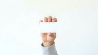 Cropped view of male hand holding blank white card against neutral background for advertising and branding purposes.