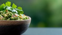 Fresh green quinoa salad with peas, herbs and vegetables in rustic ceramic bowl against blurred natural background, healthy vegetarian meal.